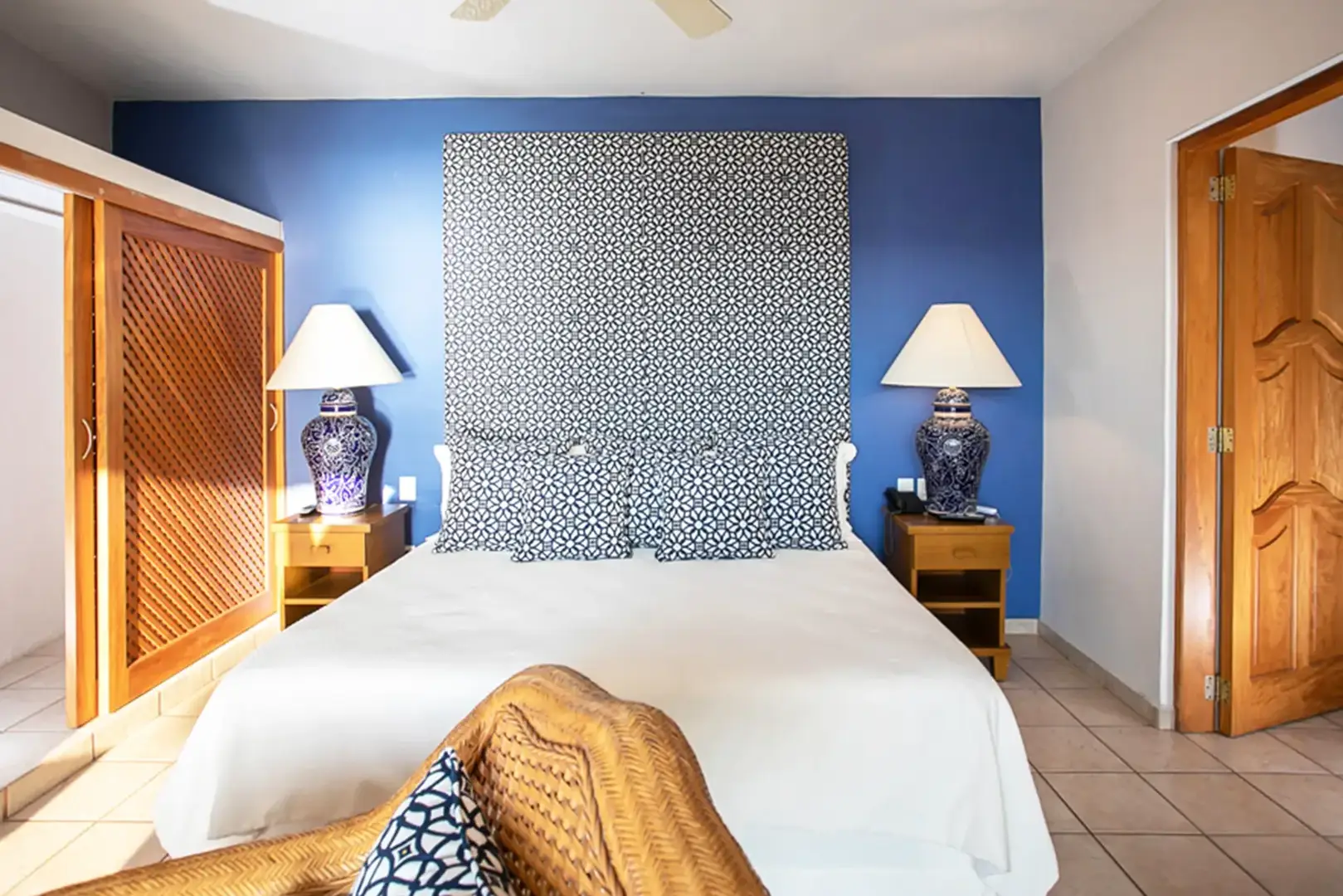 A bed with a white bedspread is centered against a blue wall, with two nightstands and blue and white lamps.